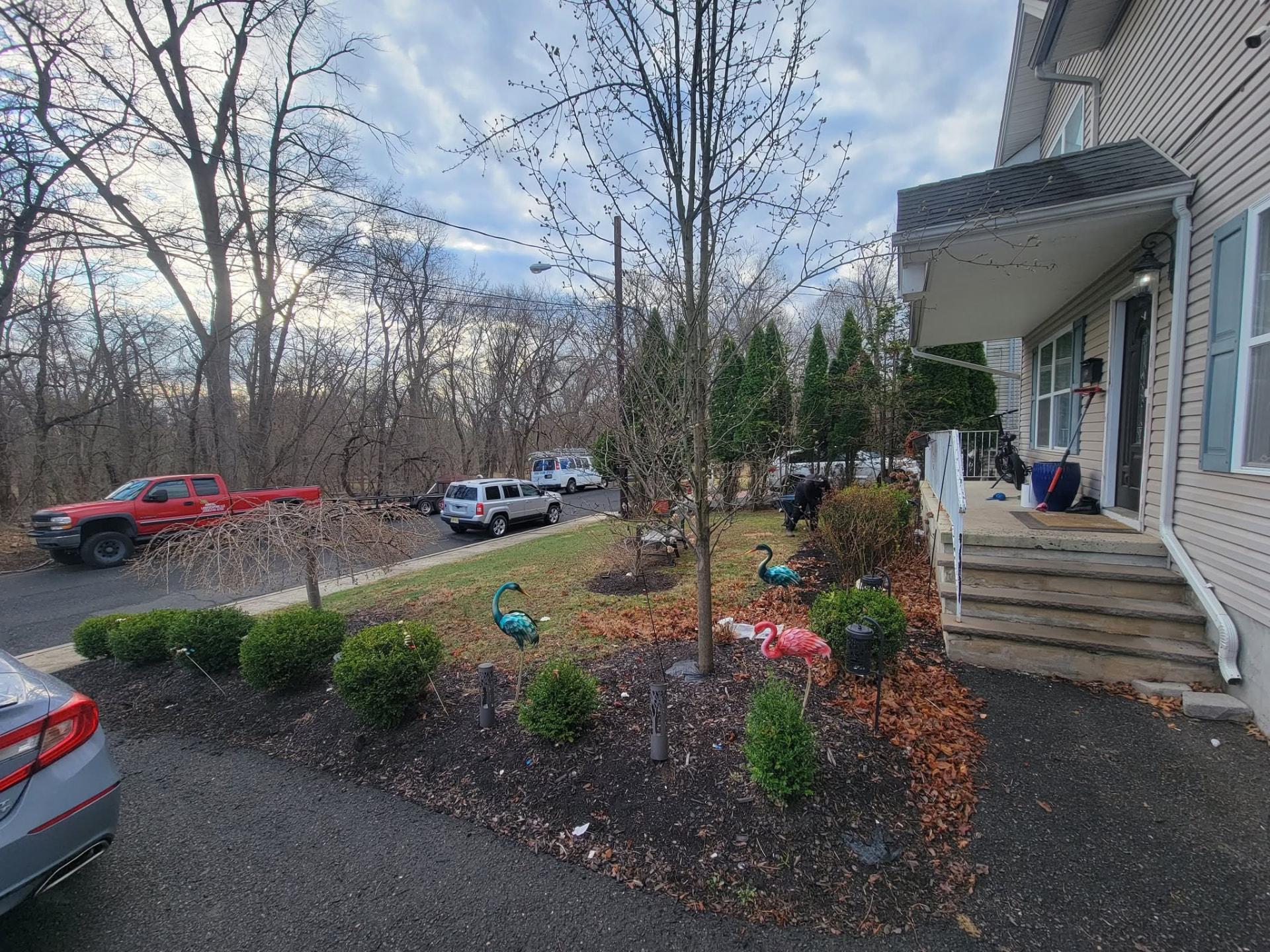 Front yard in Manville, NJ before landscaping, with patchy lawn, scattered shrubs and leaf covered beds