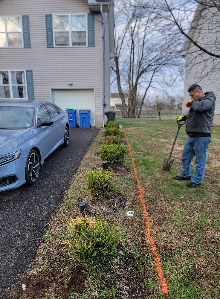 Crew member marking a new bed line with orange paint before digging along a driveway in Manville, NJ